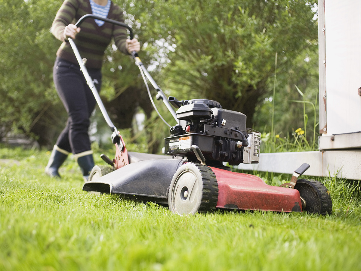 An individual uses a push mower to cut grass.
